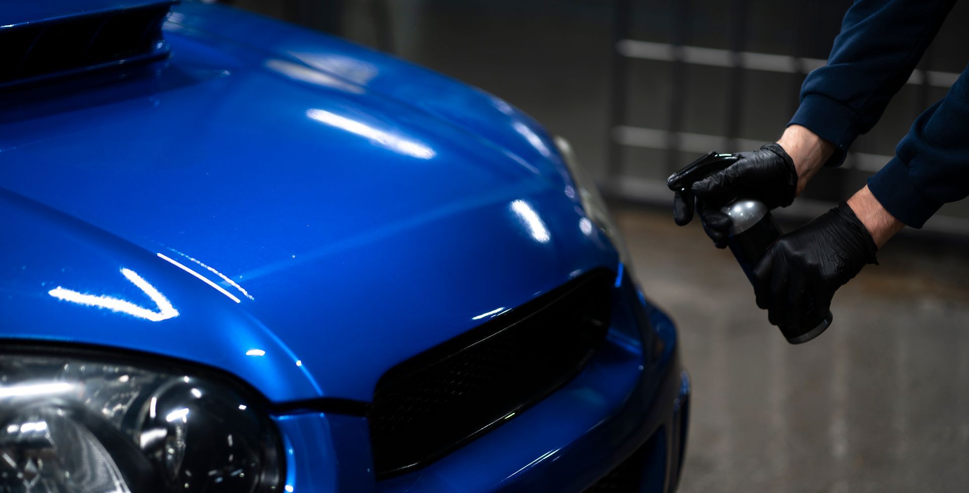 Hands in black gloves spraying blue car.