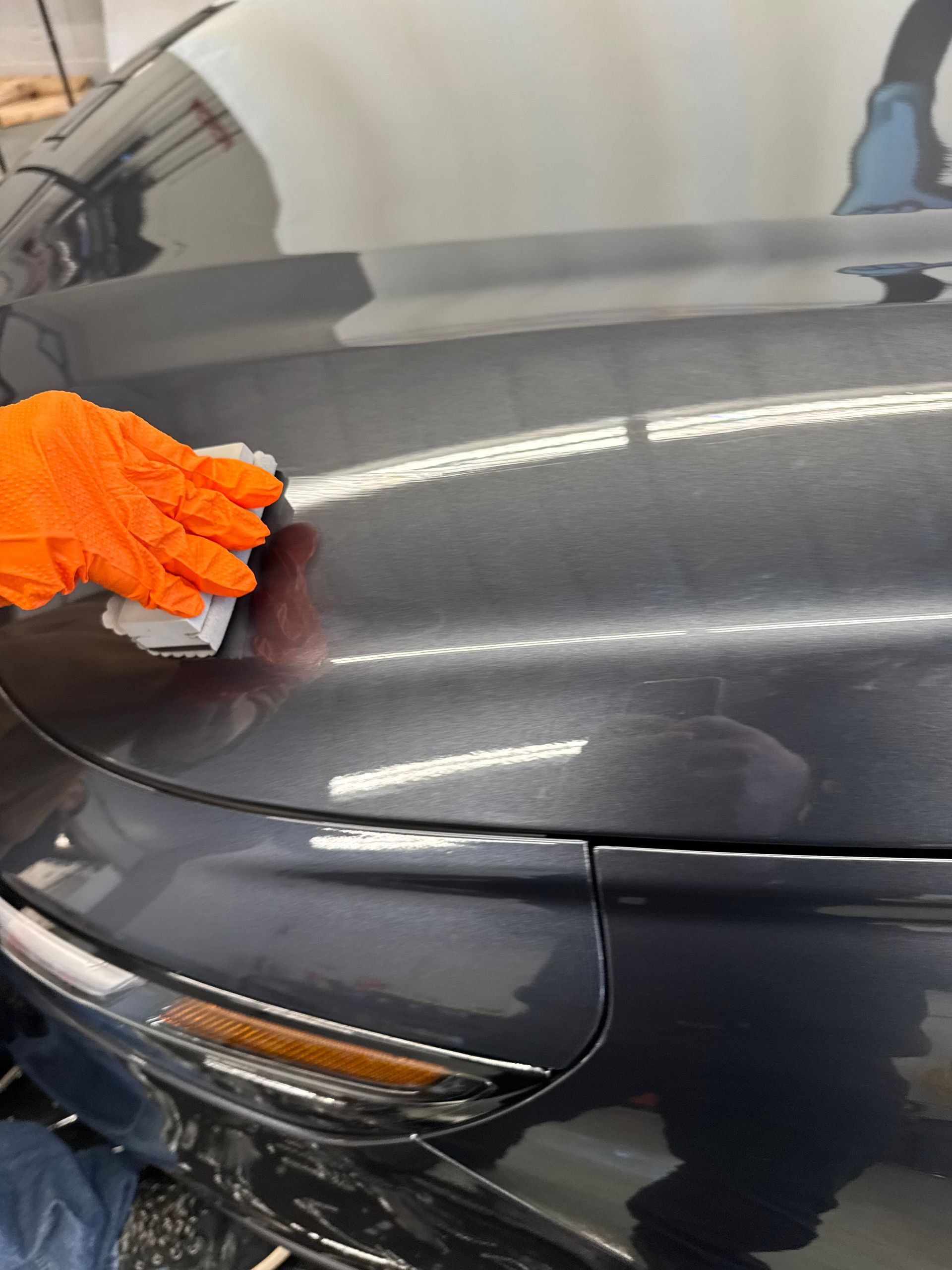 Gloved hand applying a product to a dark gray car bumper, likely detailing.