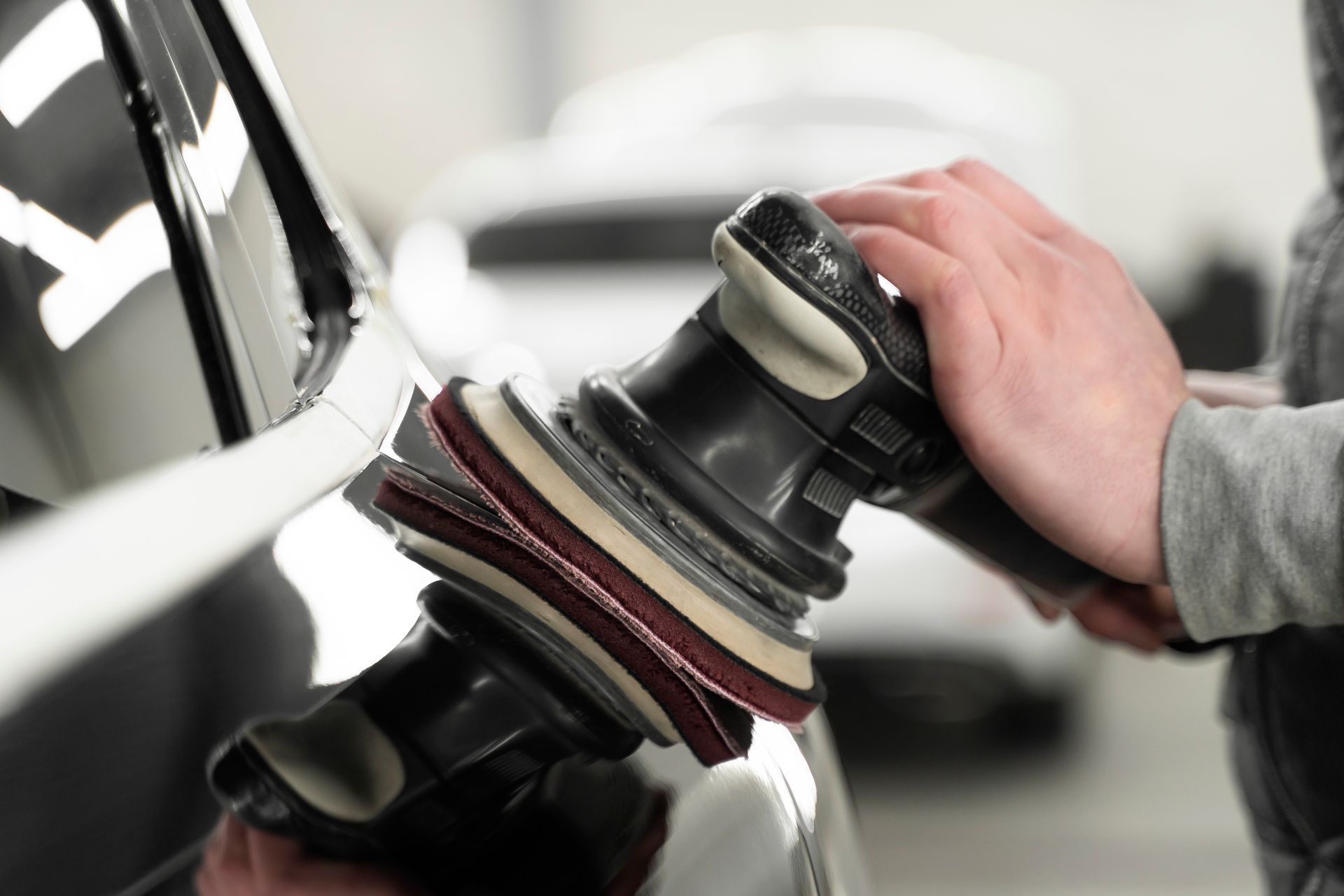 Person polishes a car with an electric buffer. Black car reflects surroundings.