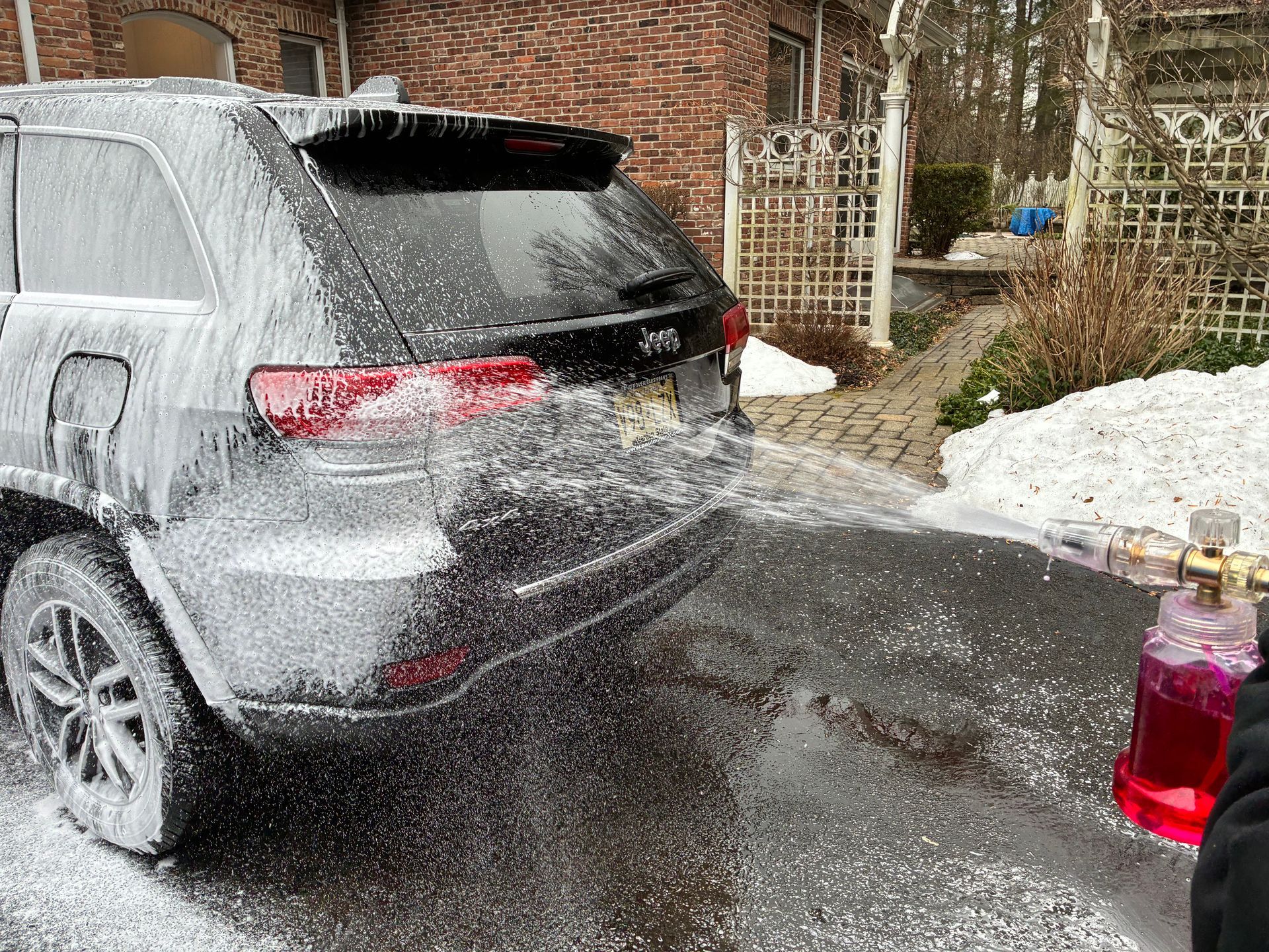 Black Jeep being covered in white foam, washing the vehicle on a driveway.