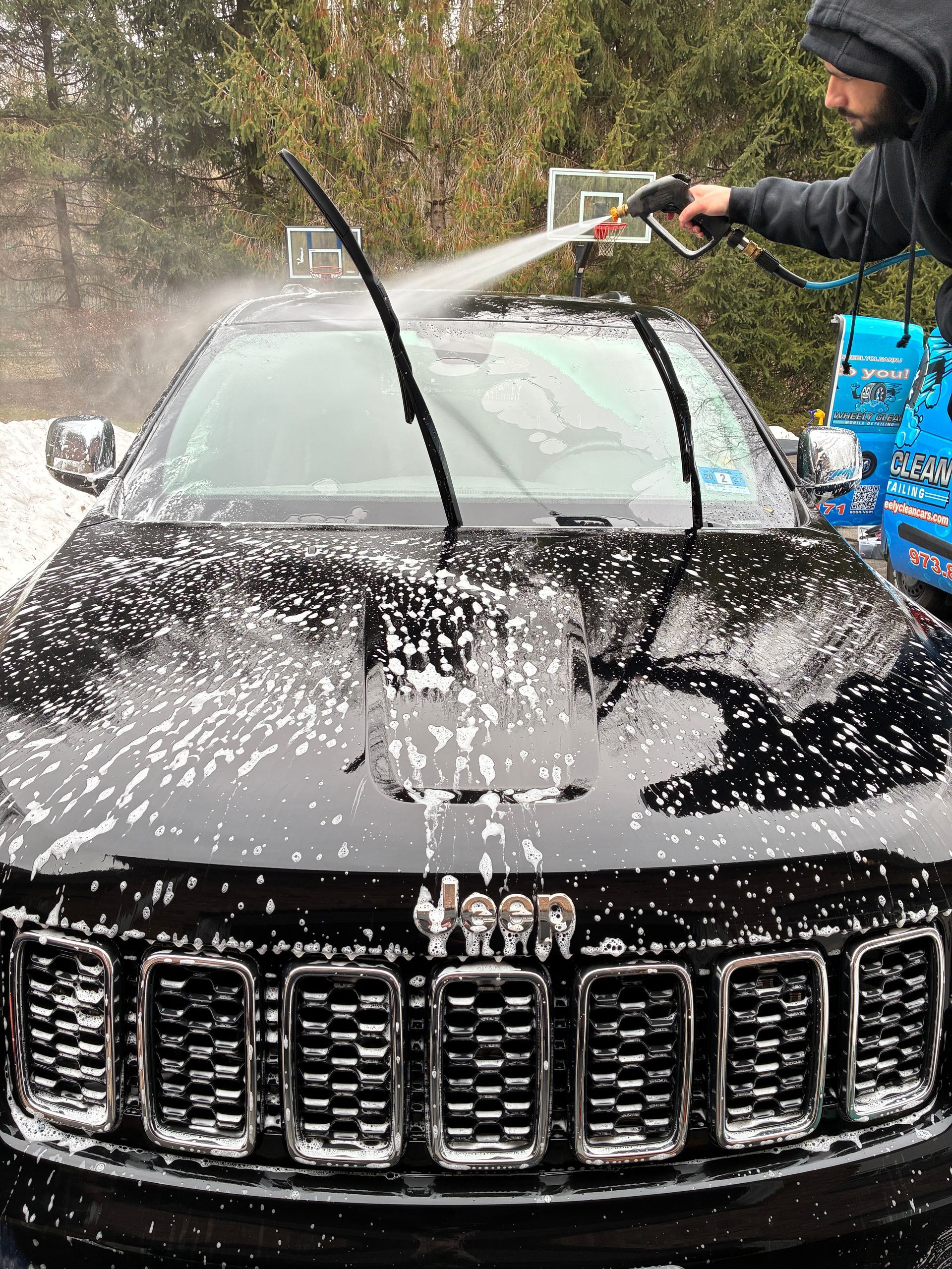 Person washing a black SUV with a pressure washer, soap covering the vehicle.