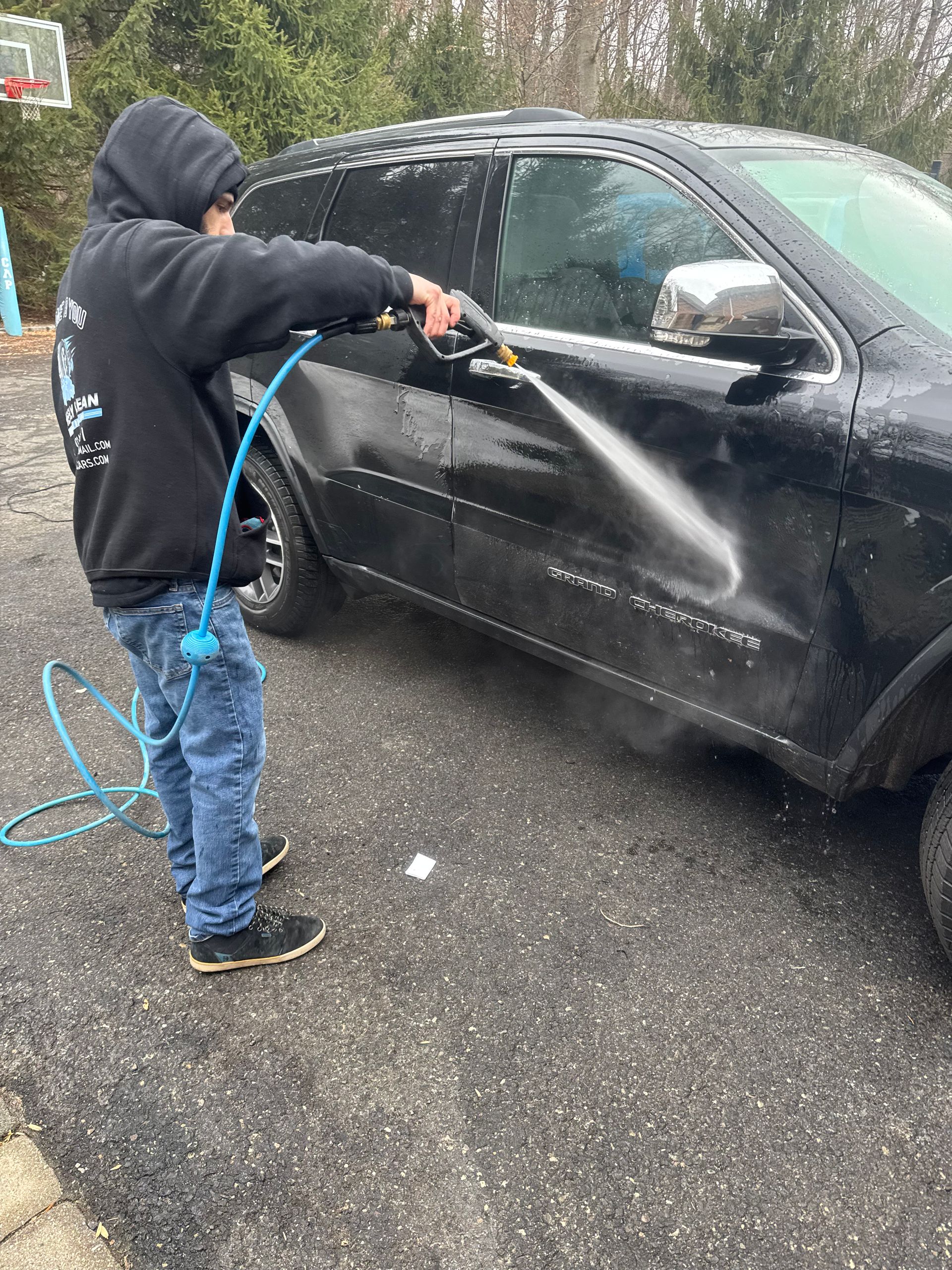 Person washing a black SUV with a hose outdoors on a paved surface.