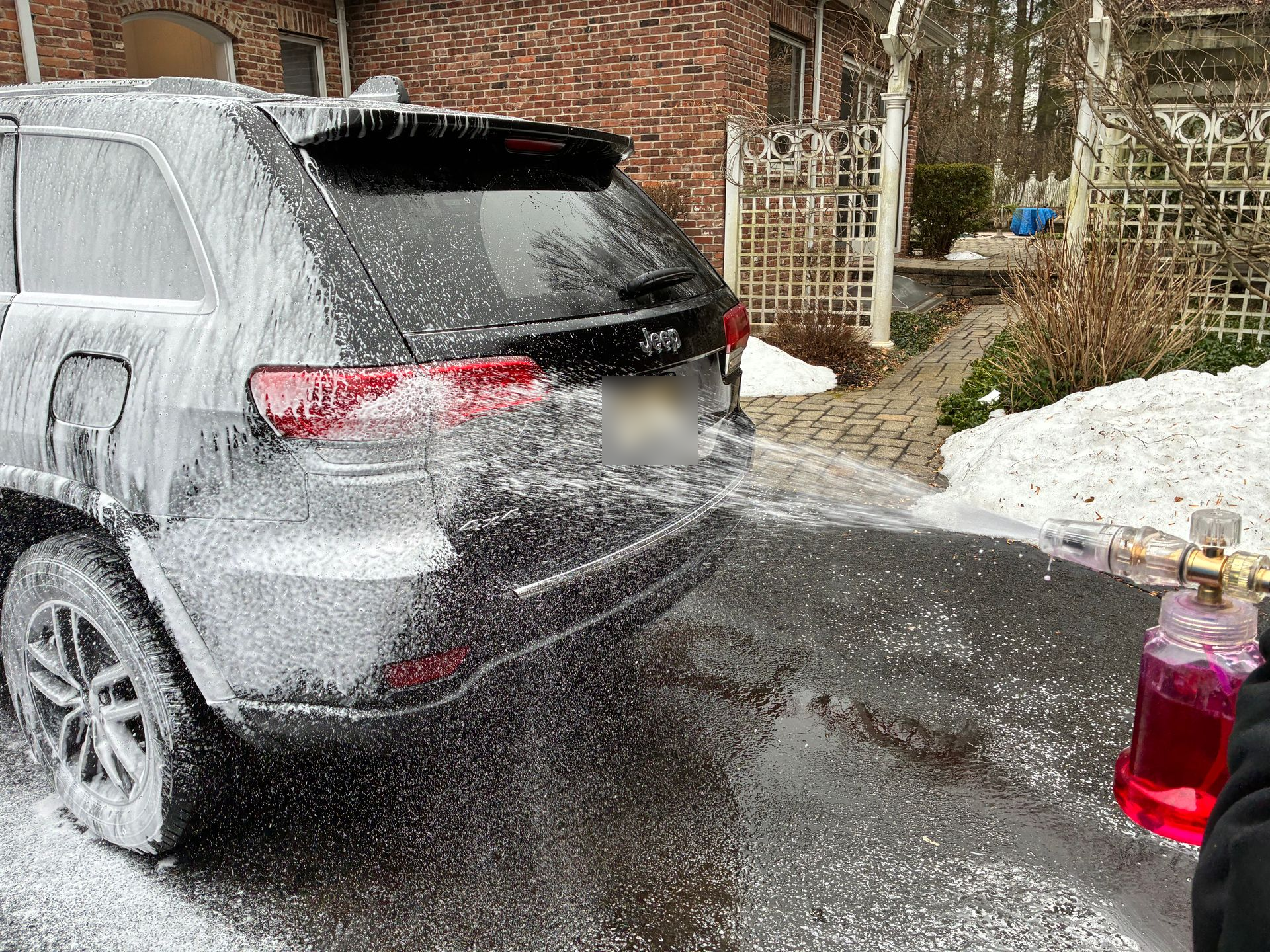 Black Jeep being covered in white foam, washing the vehicle on a driveway.