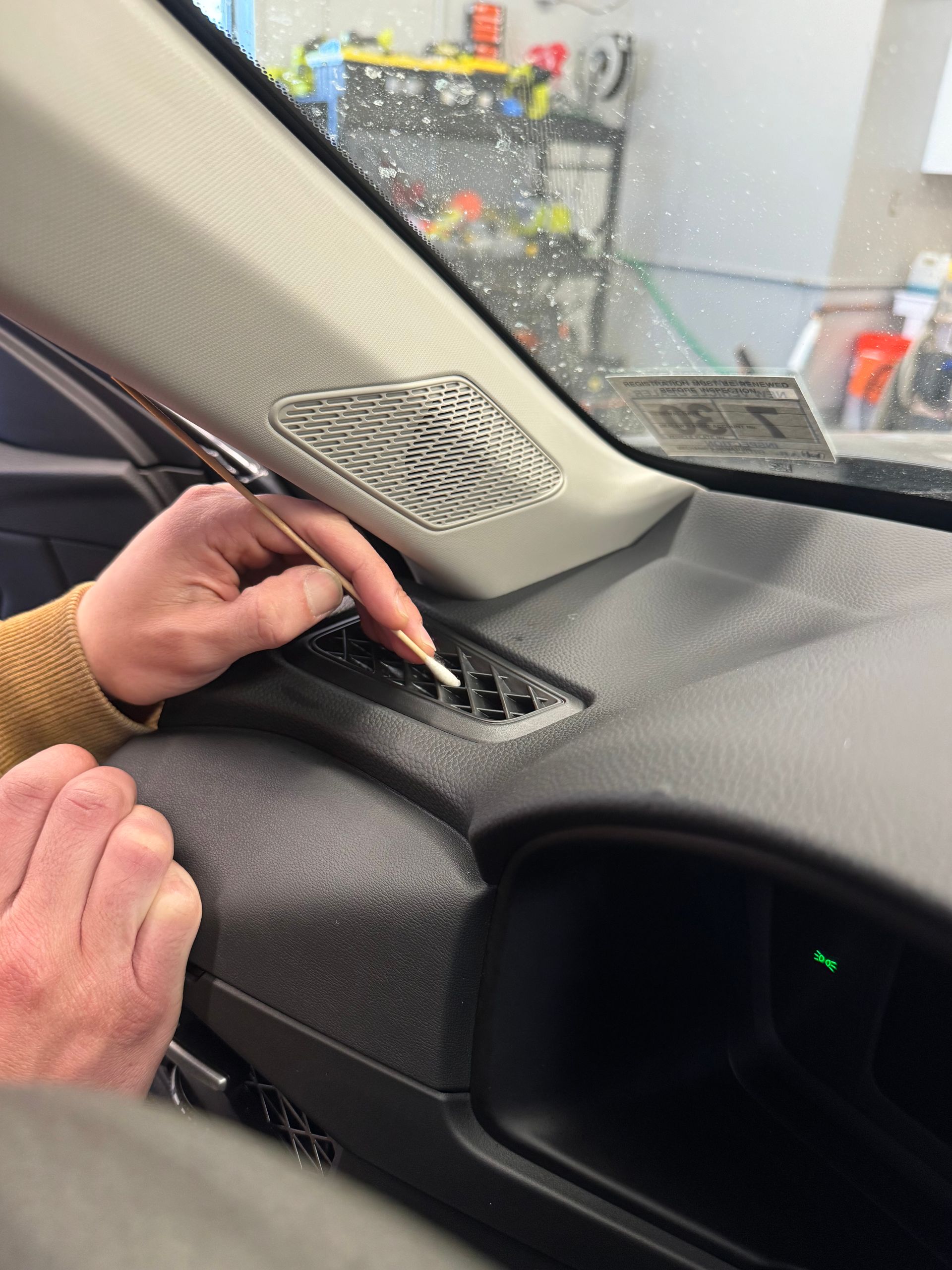 Person's hand using a tool to work on a car's dashboard vent; close-up shot.