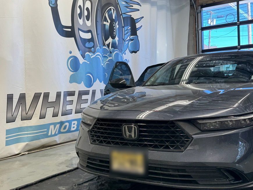 A gray Honda sedan at a car wash. The driver's door is open. Wheels Mobile logo in the background.