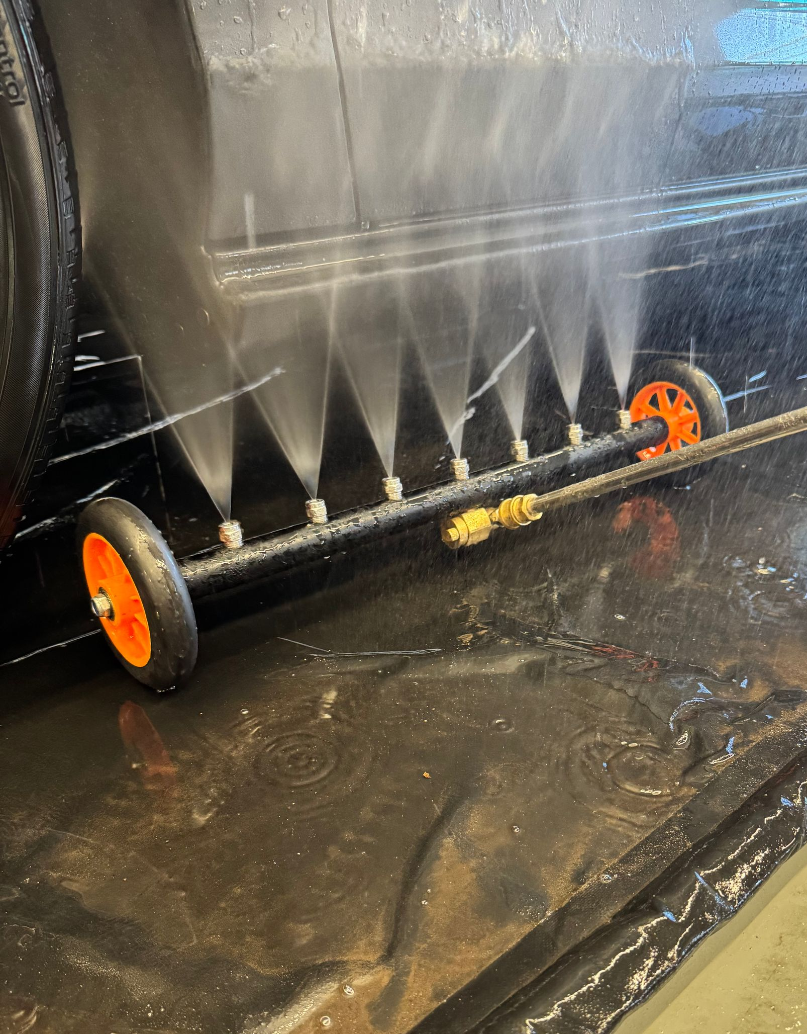 A black surface being cleaned with a wheeled spray bar, water jets visible.