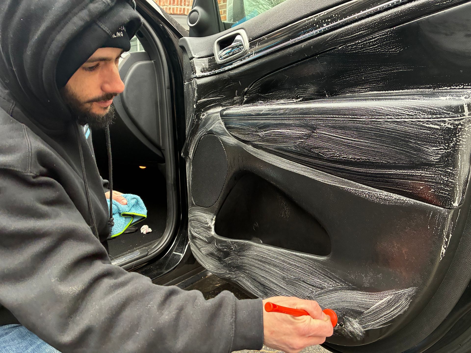 Man cleaning a car door's interior with a brush. Black door panel, suds visible.