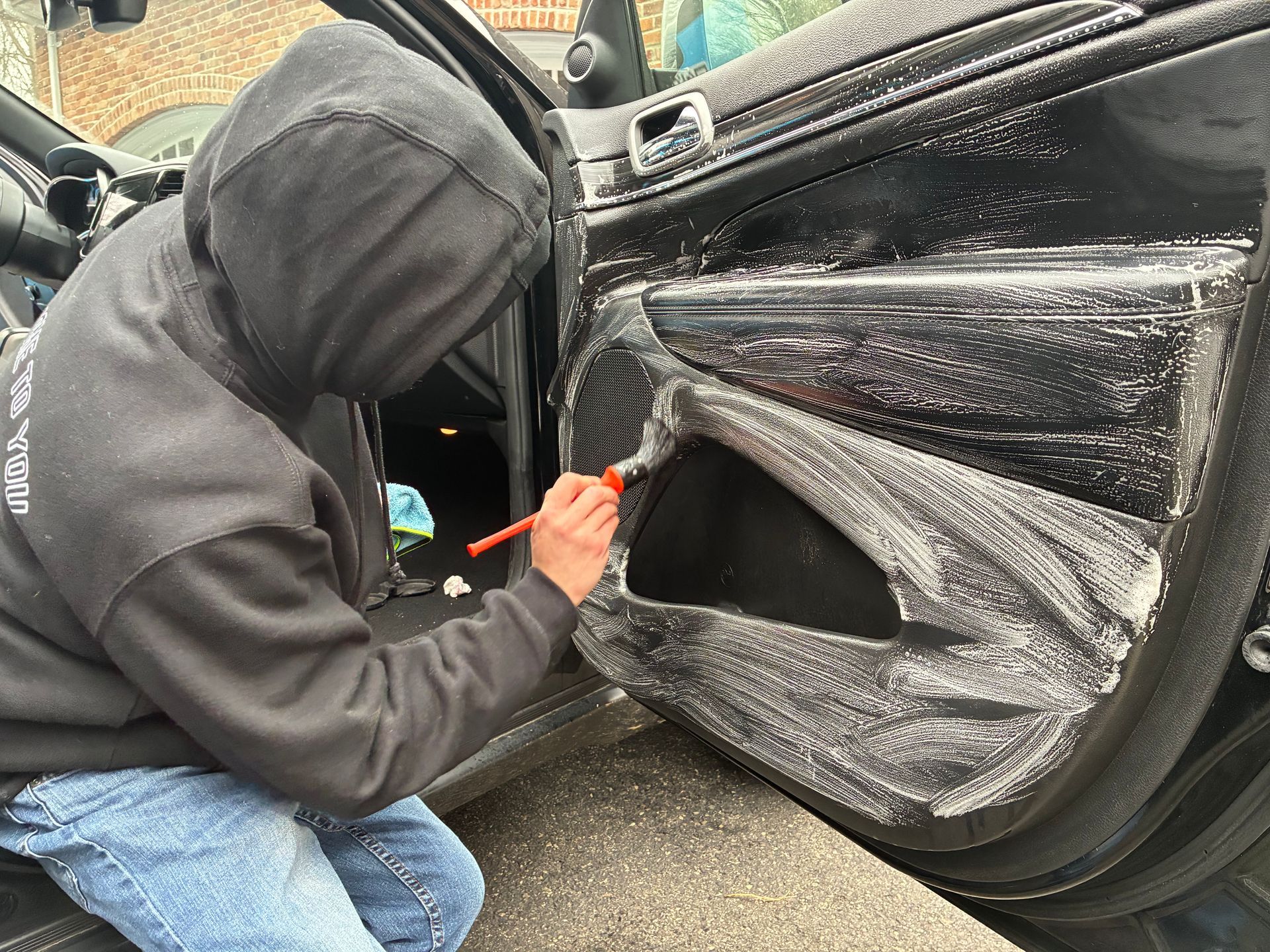Person in hoodie using a tool to apply film to a car door.