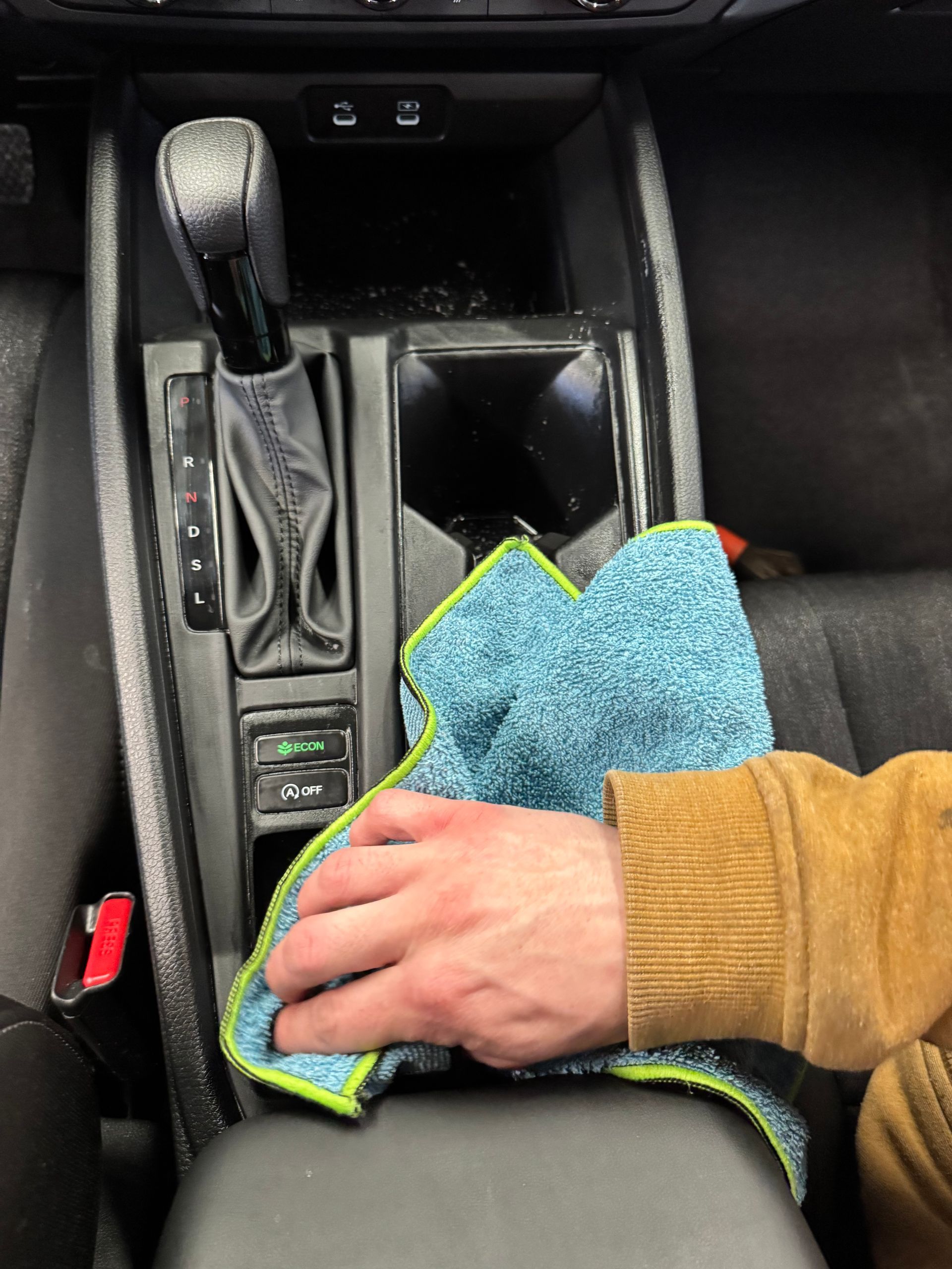 Hand wiping interior car console with a blue microfiber cloth.