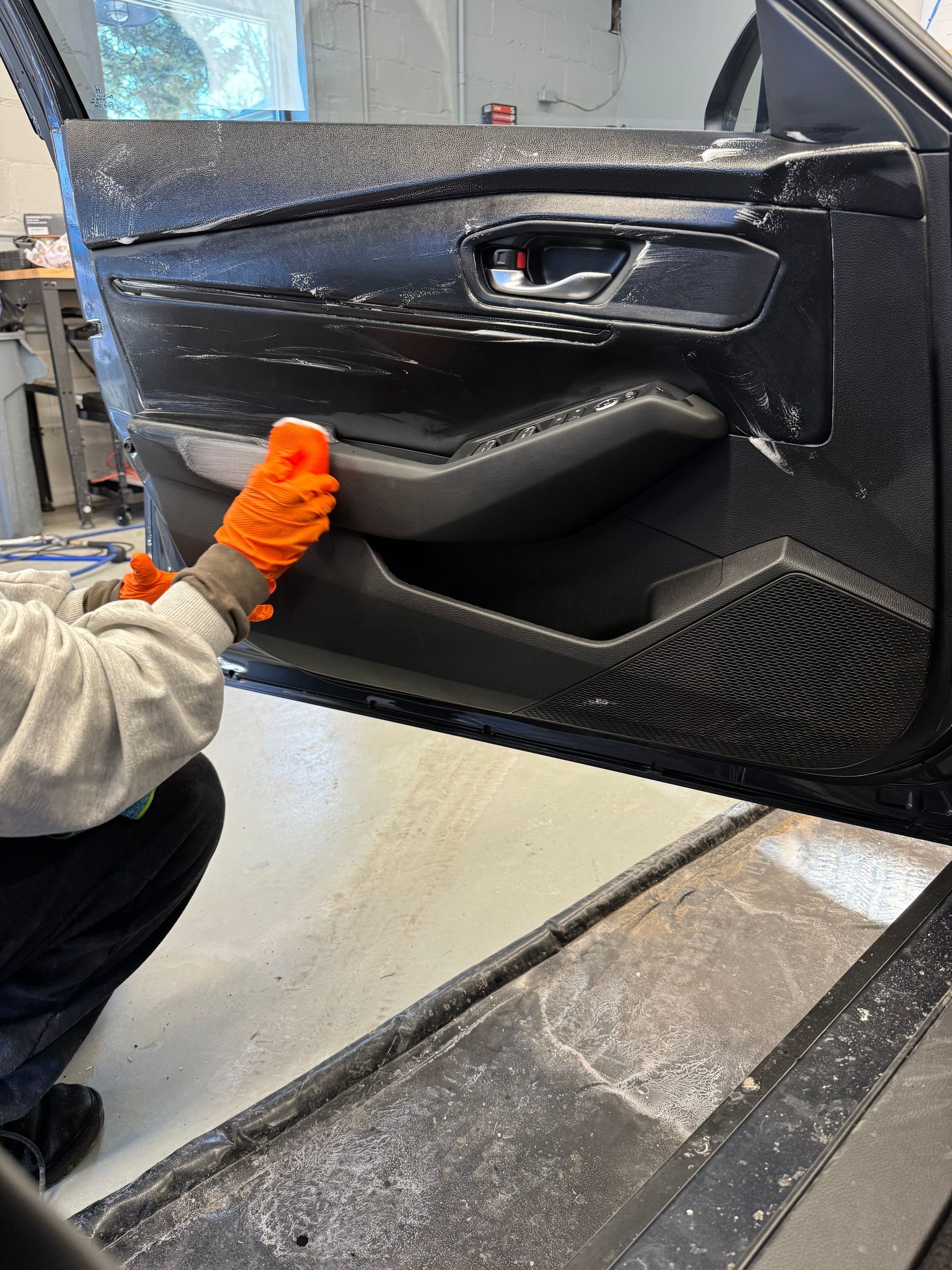 Person wearing orange gloves working on a black car door in a garage.