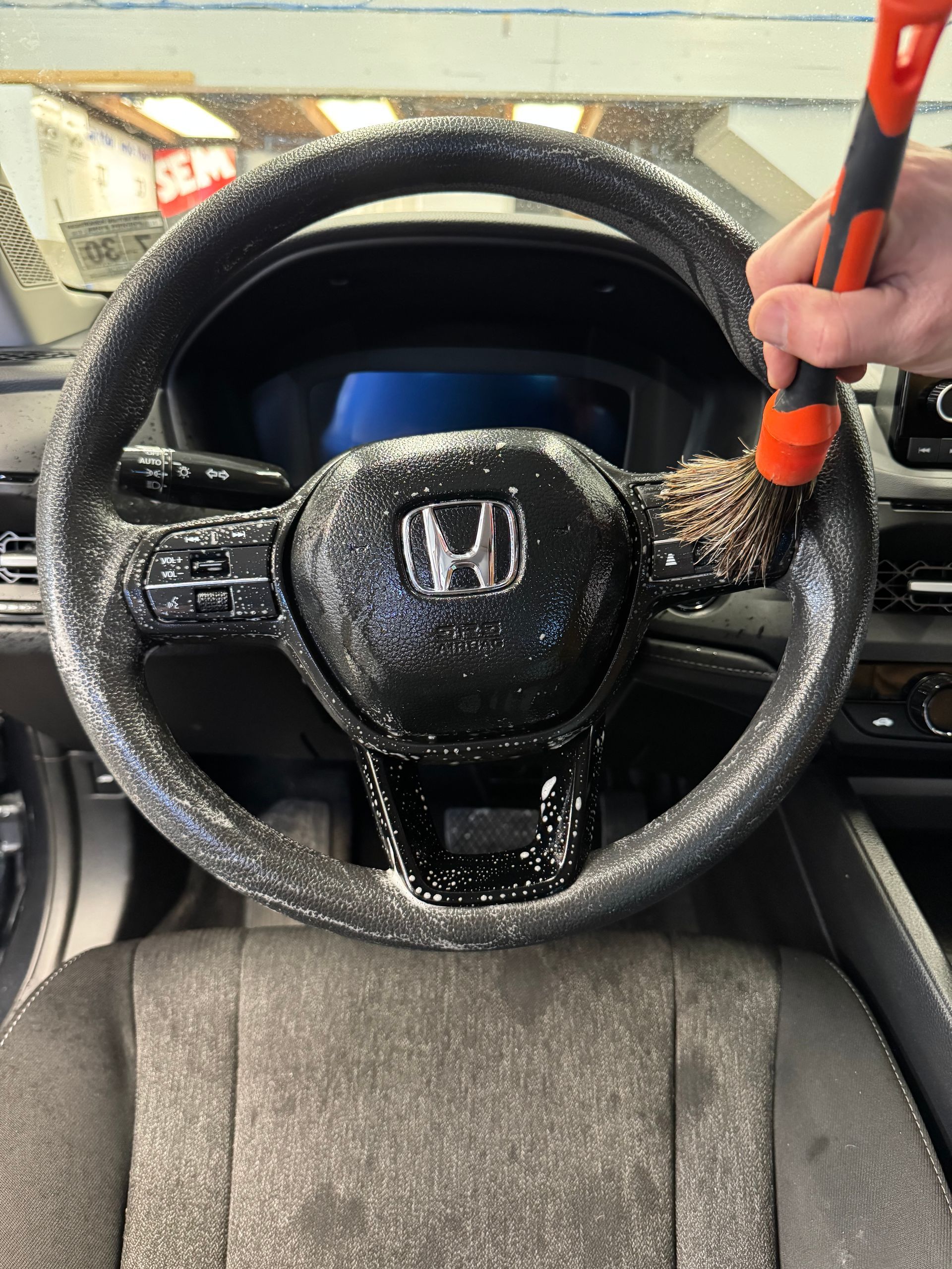 Cleaning a black Honda steering wheel with a brush.