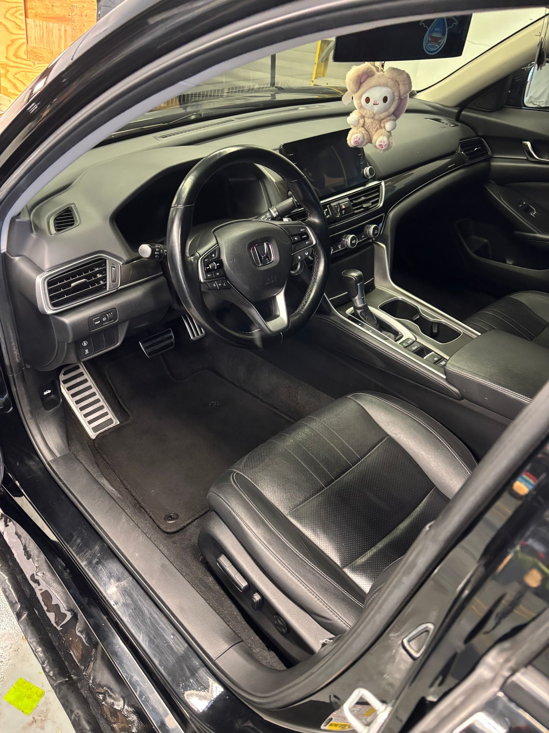 Black car interior with steering wheel, dashboard, seats, and floor mats.
