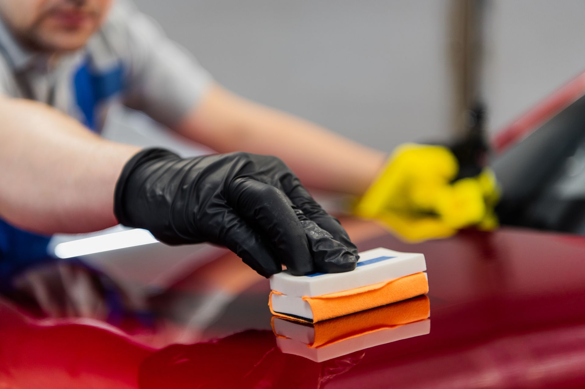 Person applying ceramic coating to a red car using an applicator pad, wearing black gloves.