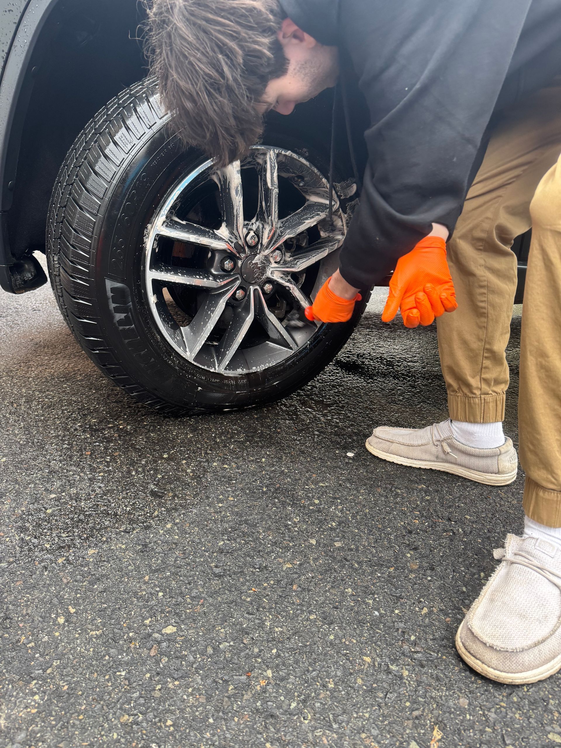 Person wearing orange gloves cleaning a car tire with cleaning products.