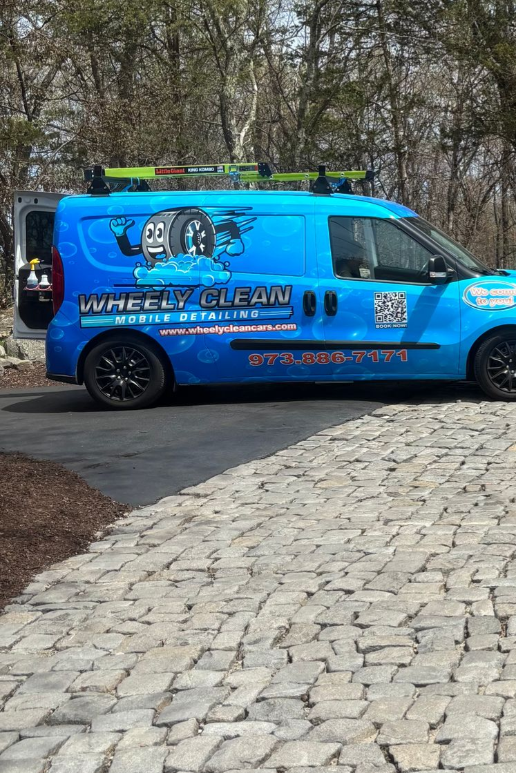 Blue van and black truck parked on a cobblestone driveway near a building with a stone exterior.