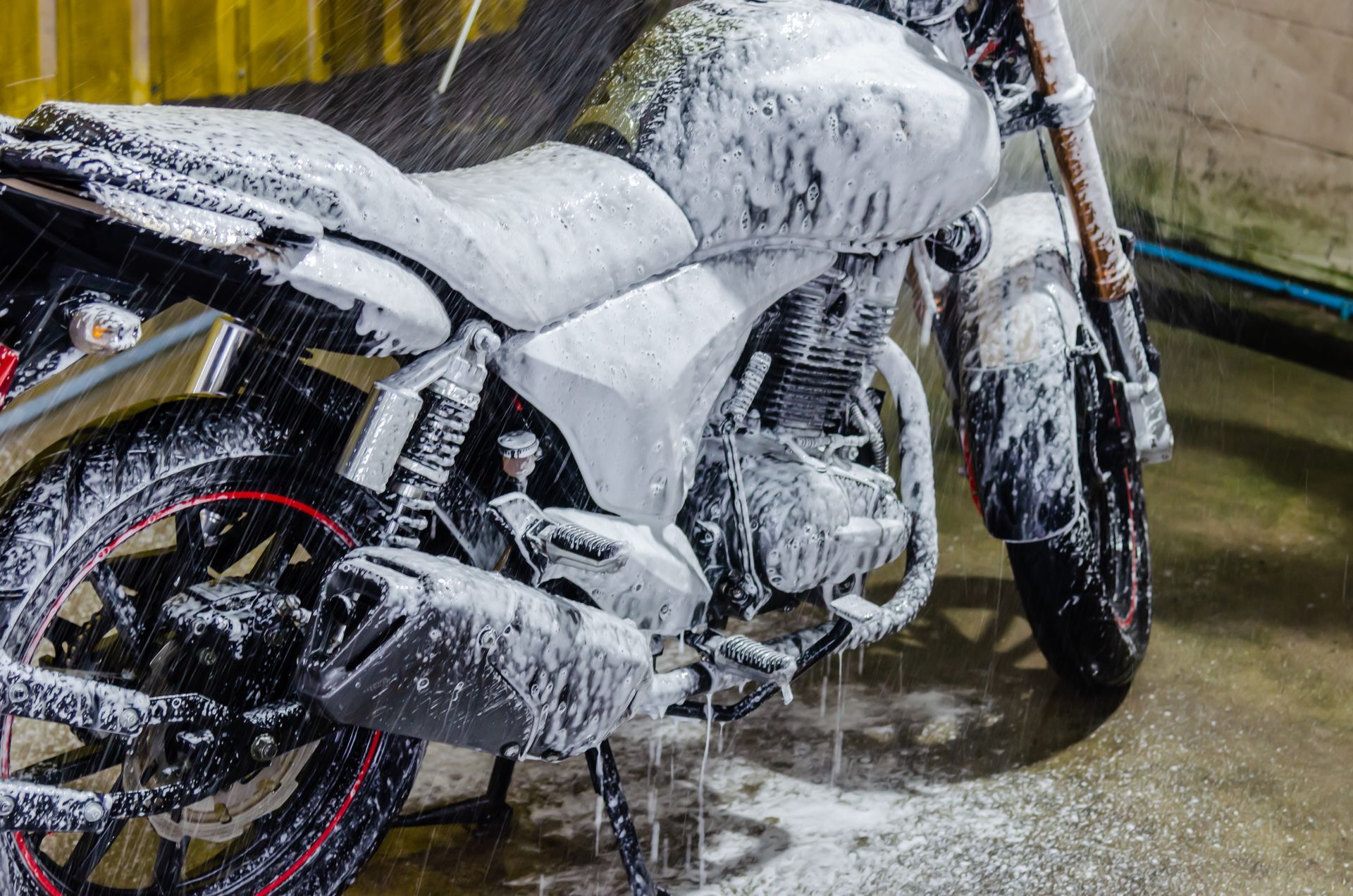Motorcycle covered in white foam, being washed. Black tires with red rims in a garage setting.