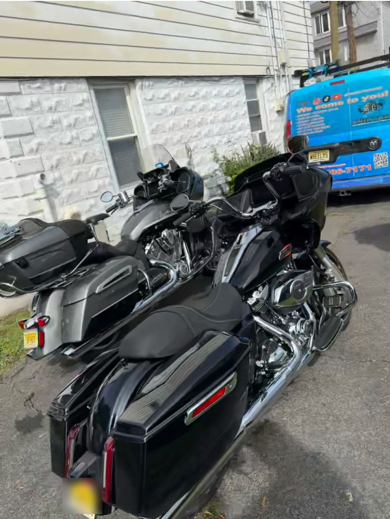 Two touring motorcycles parked on a street near a building and a van.