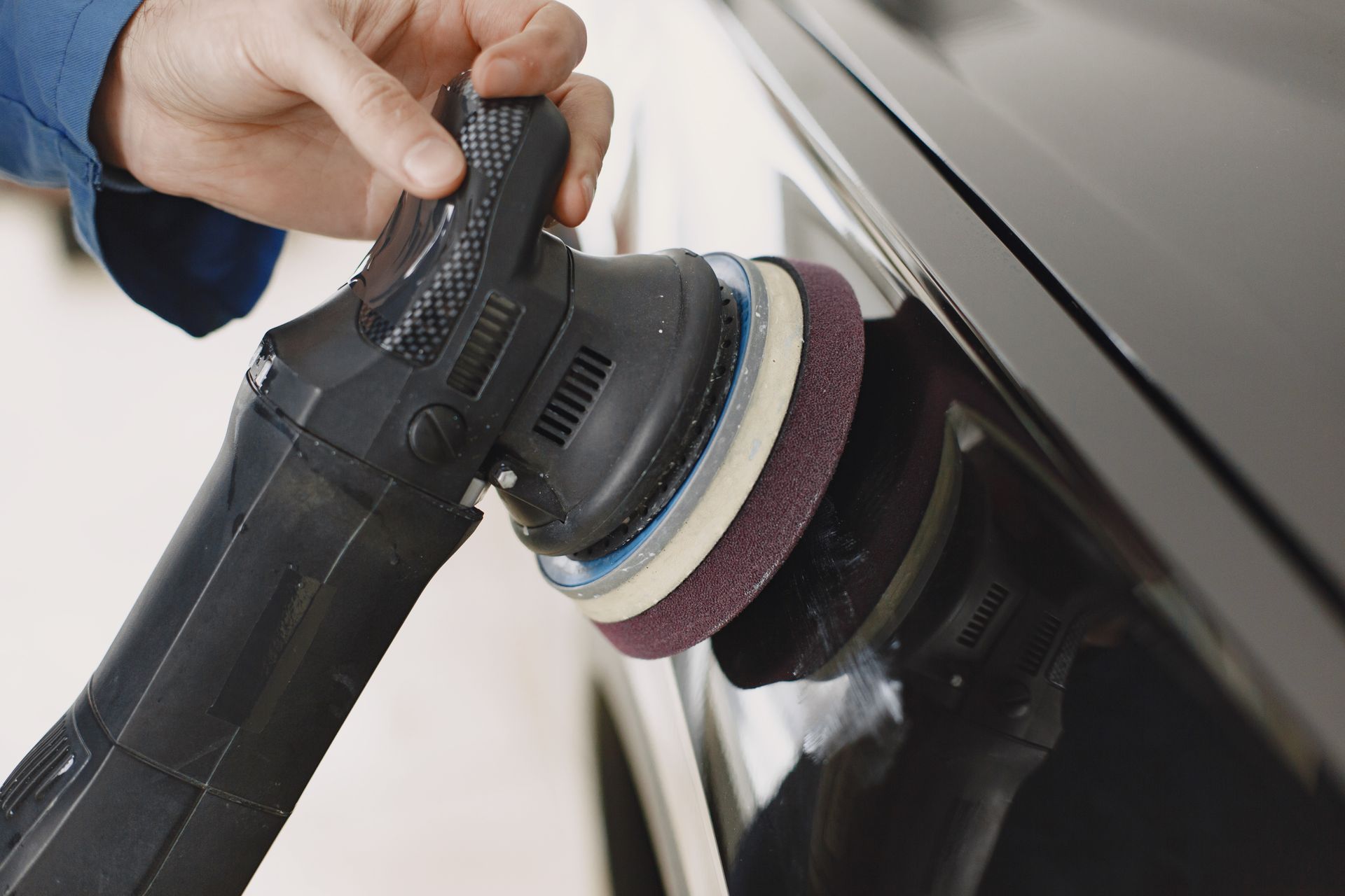 Person using an electric polisher on a black car, buffing the paint.
