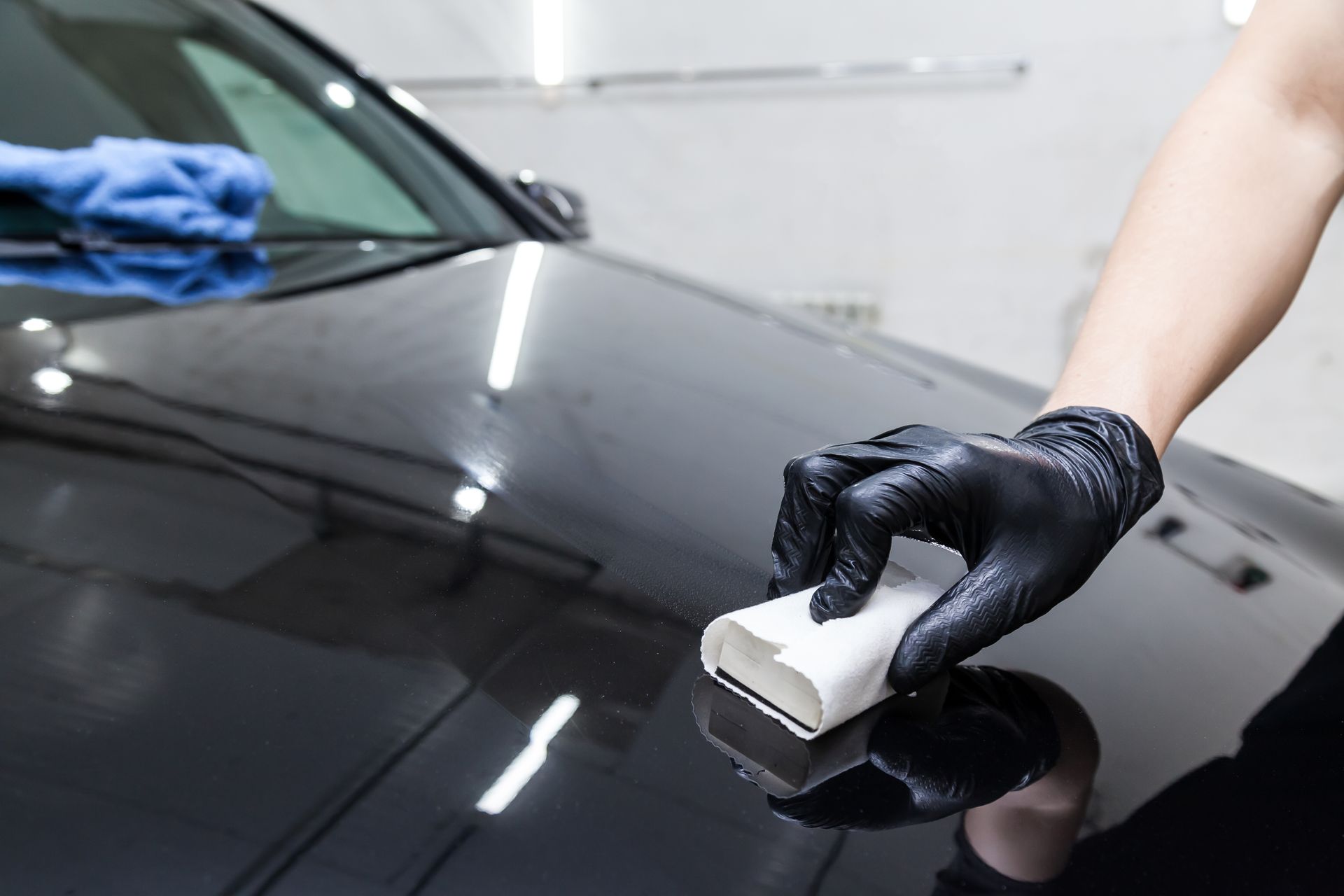 A person in black gloves applying a ceramic coating to a shiny black car hood.