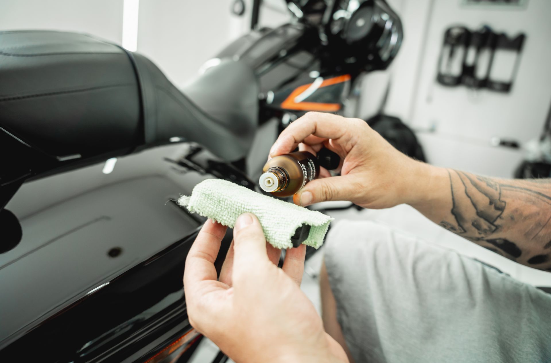 Person applying ceramic coating to a black motorcycle, indoors, using a cloth and bottle.