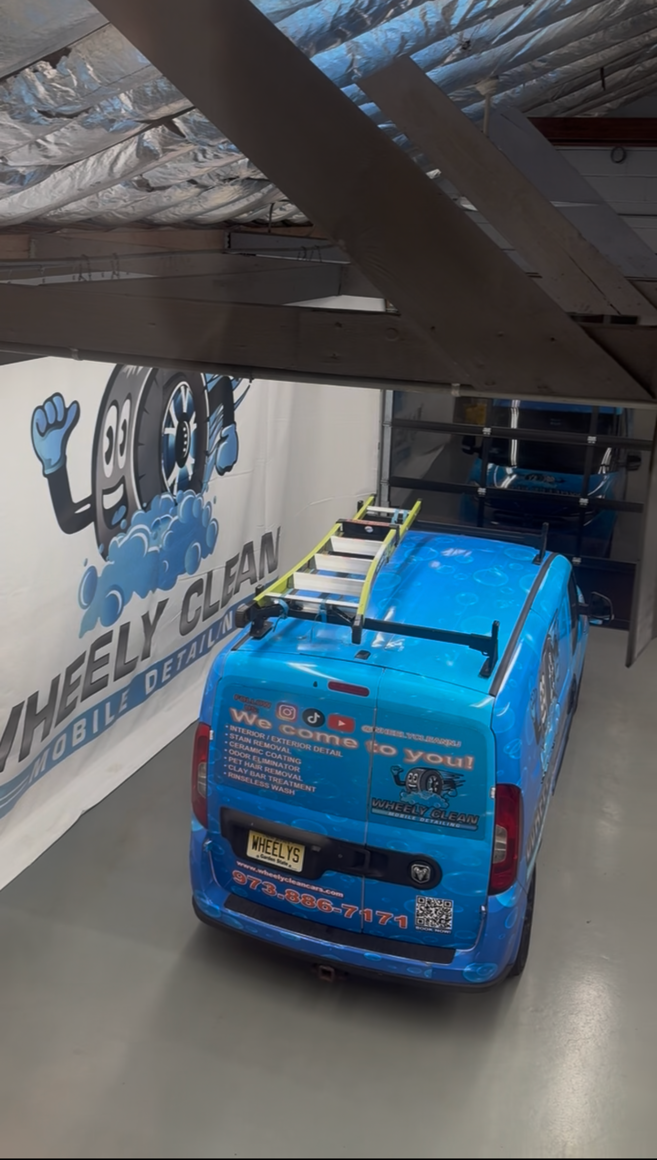 Blue van with a ladder parked inside a car wash bay, with