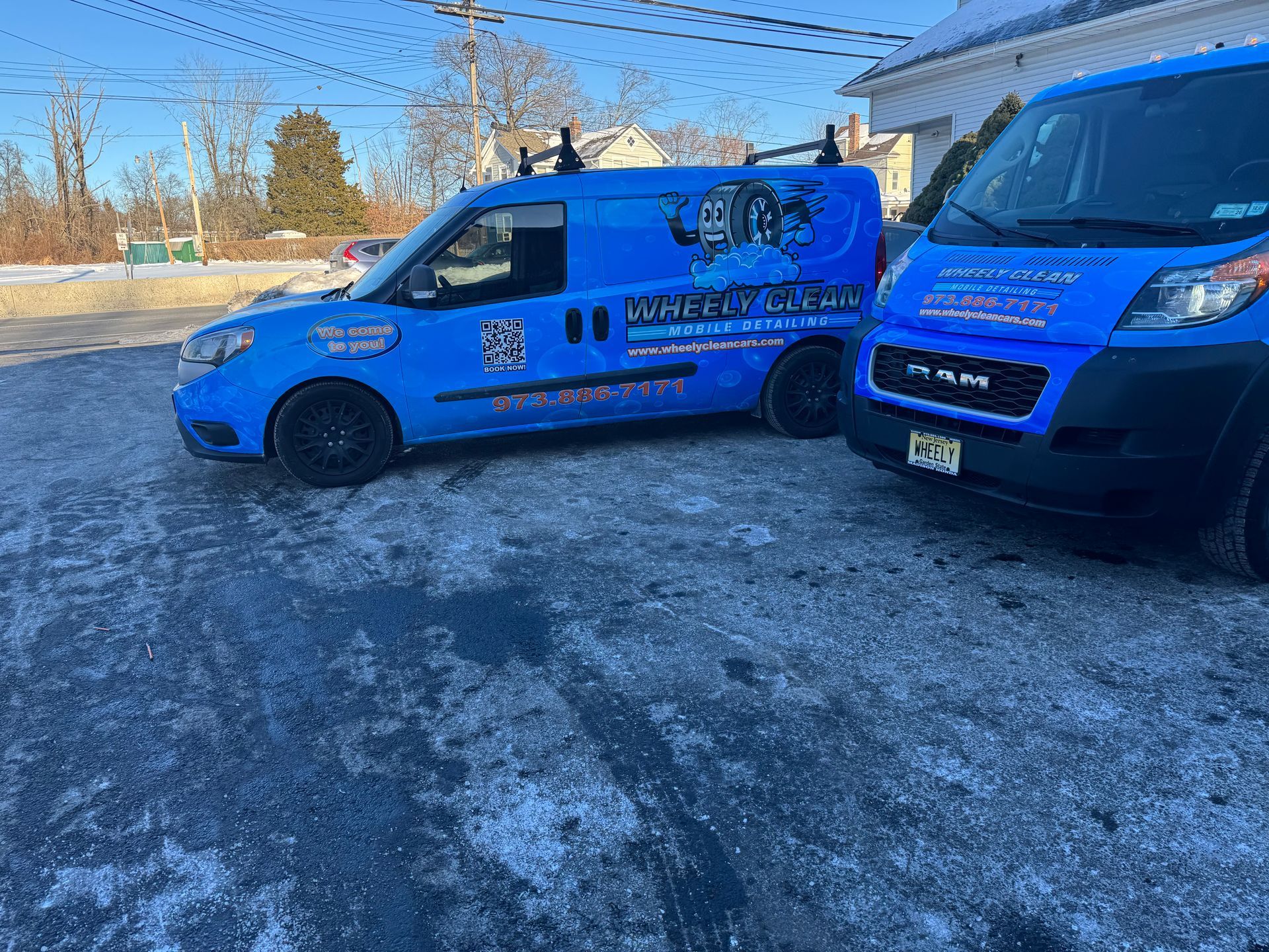 Two blue vans with business logos parked on a snowy lot.