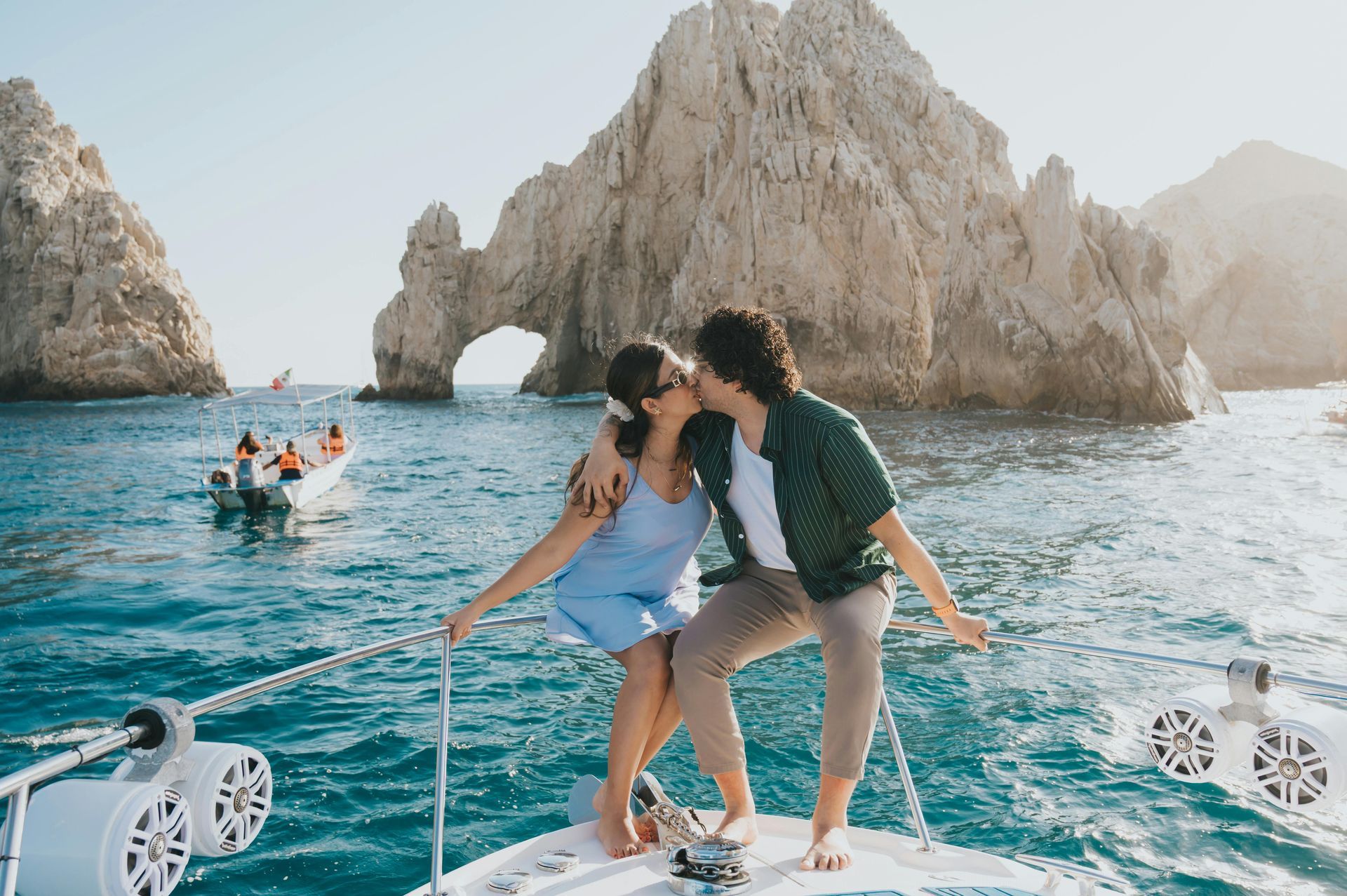 Couple kissing on a boat with rock formations in the background, blue water and sunny day.