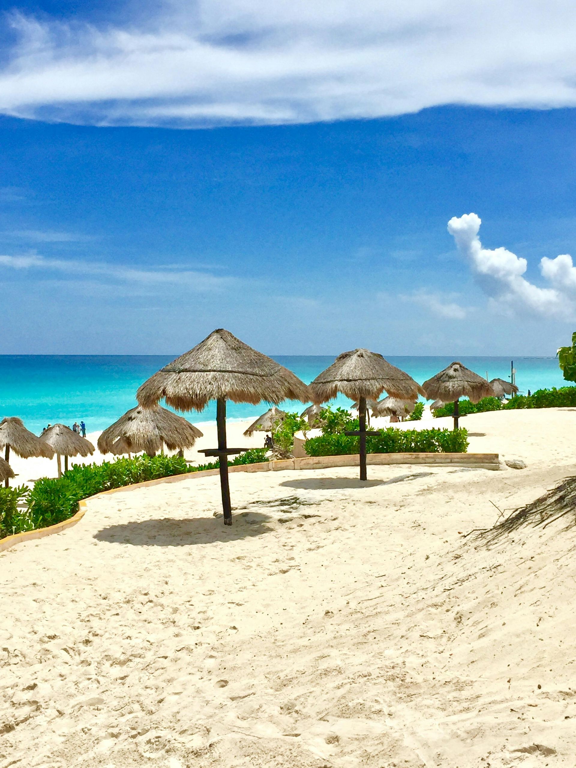 A scenic view from a wooden platform overlooking a turquoise Caribbean beach with cliffs, lush greenery, and small boats.