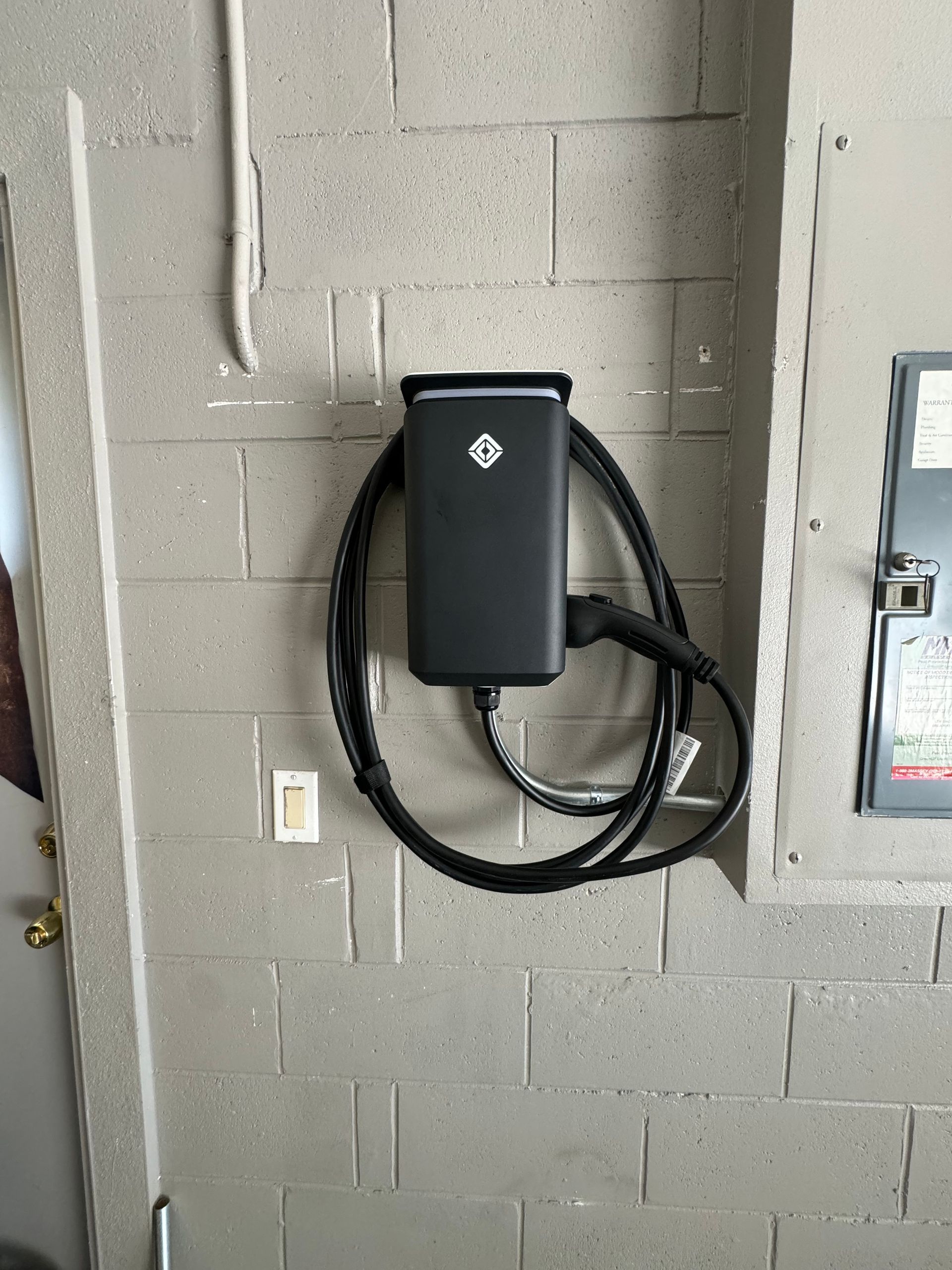 A black charger is hanging on a brick wall.