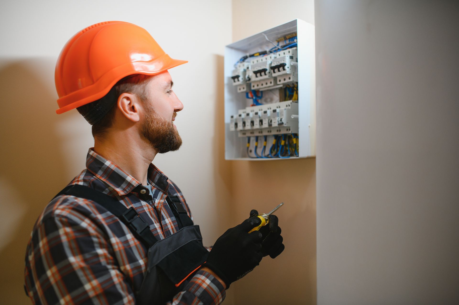 A man wearing a hard hat is working on an electrical box.