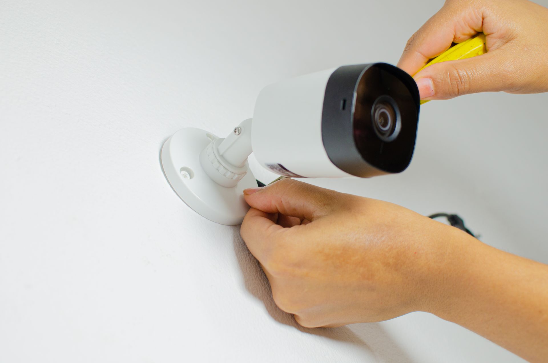A person is installing a security camera on a wall.