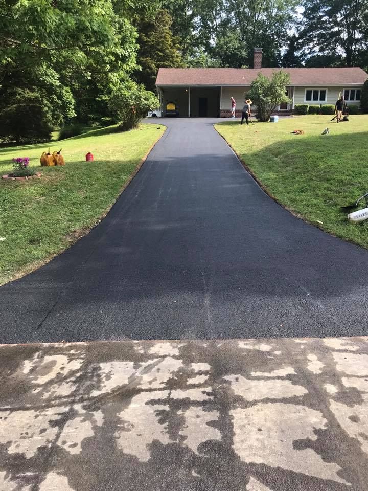 Newly paved asphalt driveway leading to a ranch-style house with green grass on either side.
