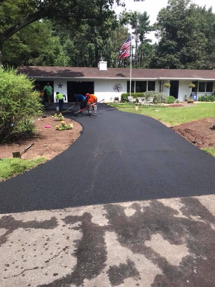 Freshly paved asphalt driveway leading to a white house with workers visible.