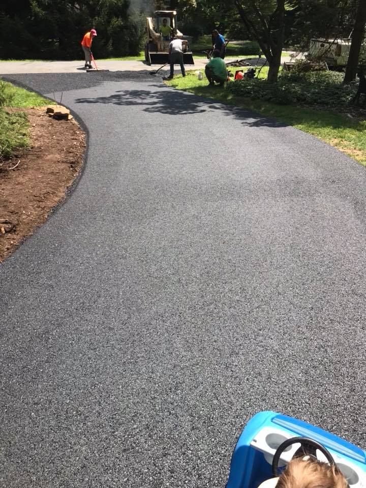 Newly paved asphalt path with workers in background; blue toy car in foreground.