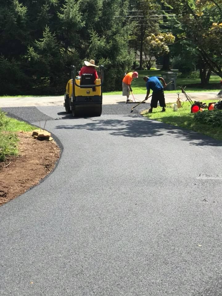 Asphalt paving a driveway. Workers operating a roller and rakes. Sunny day.