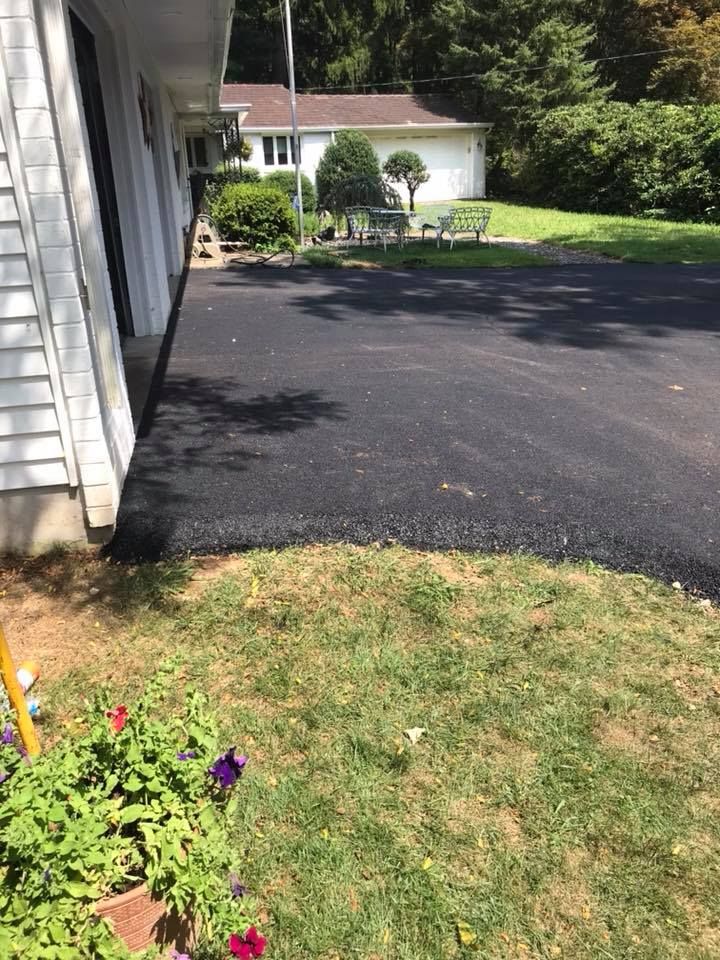 Freshly paved black asphalt driveway alongside a white house and green lawn.