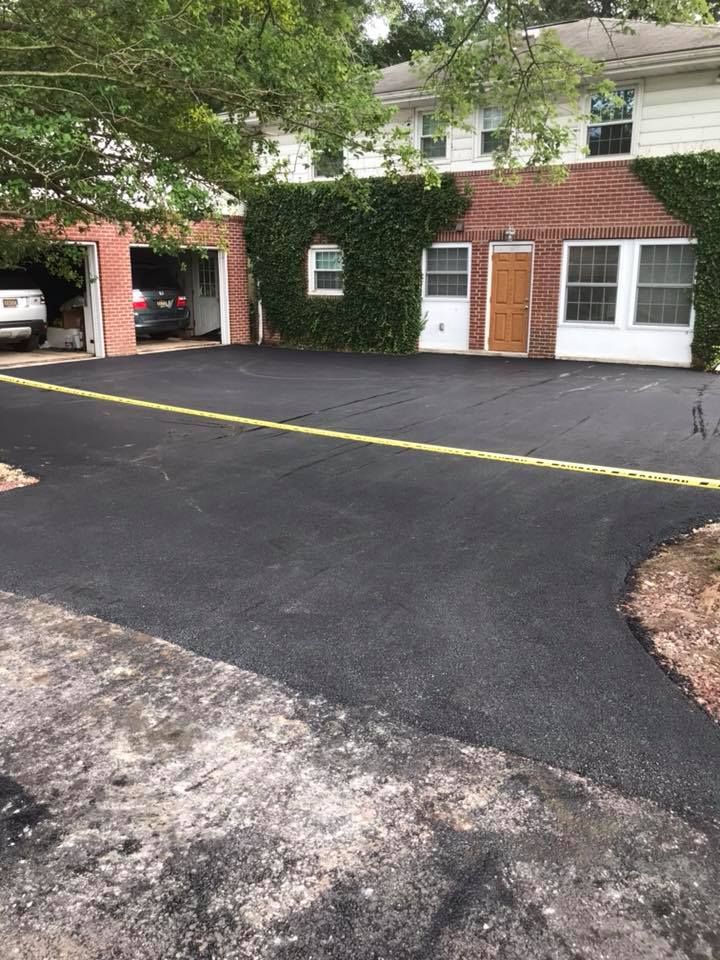 Newly paved asphalt driveway leading to a brick building with garage and ivy-covered wall.