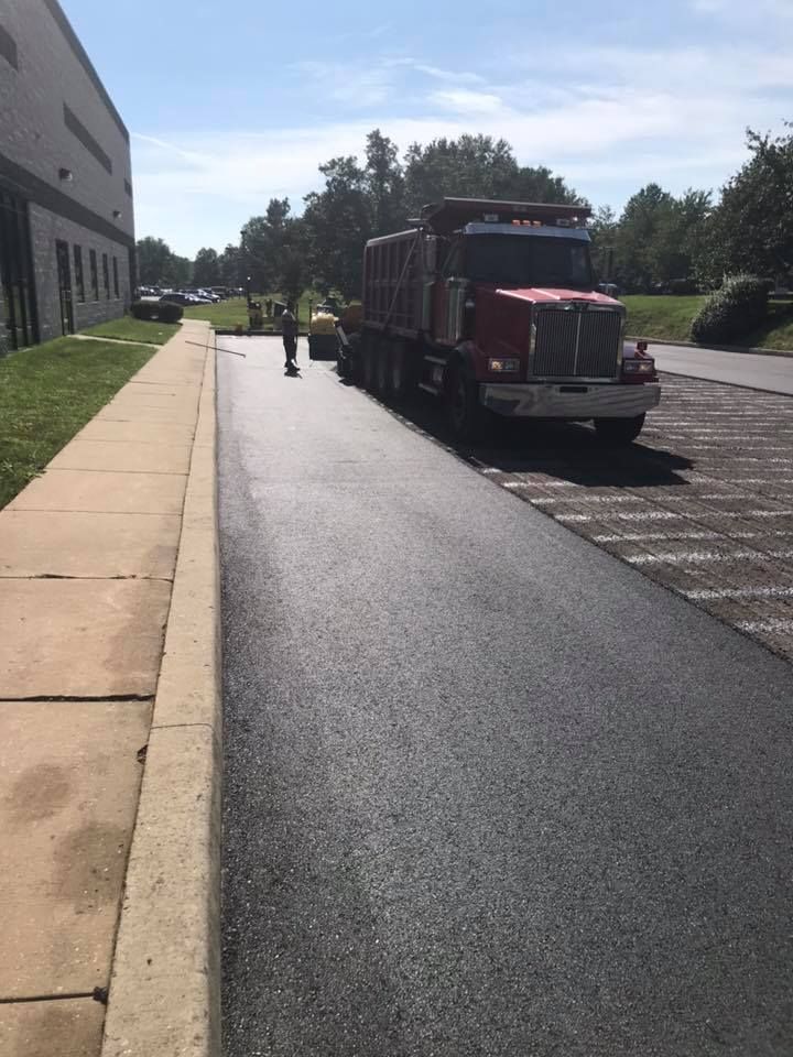 Asphalt paving in progress next to a building. Dump truck parked, worker near the truck.