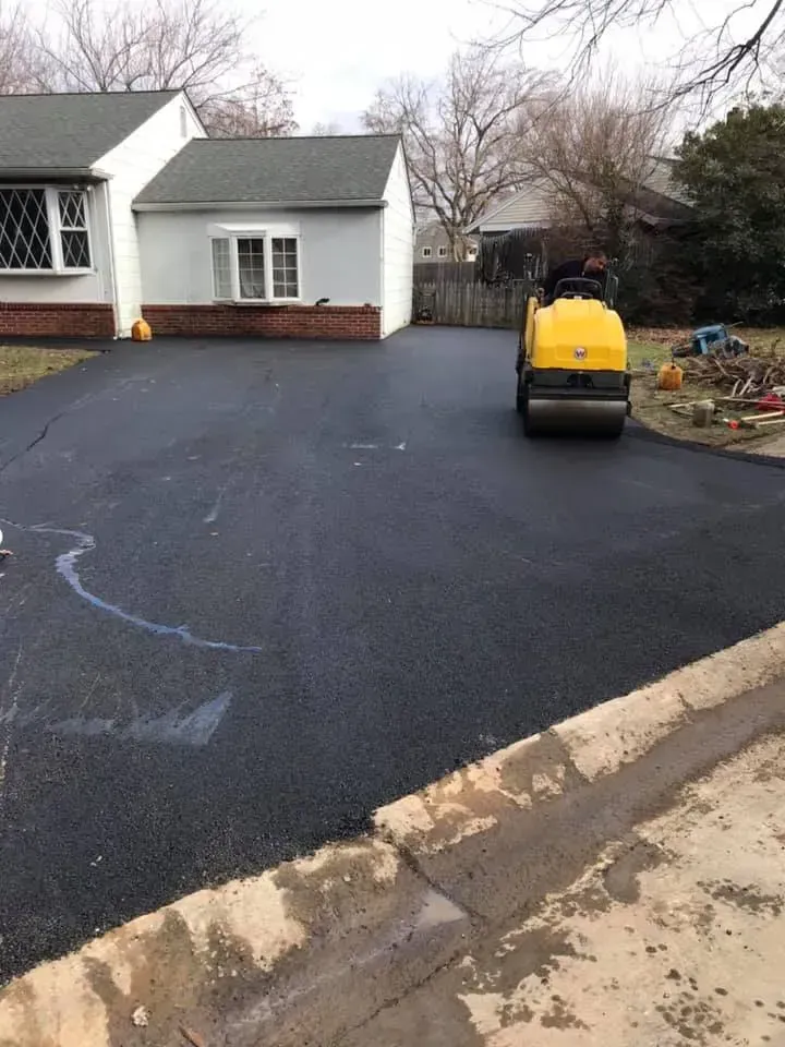 Asphalt driveway being rolled by a construction worker, house in background.