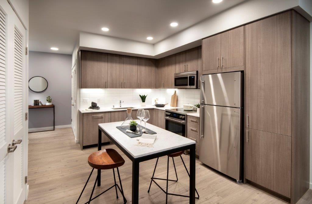 Modern apartment kitchen with center island, stainless steel appliances, and wood-tone cabinets.