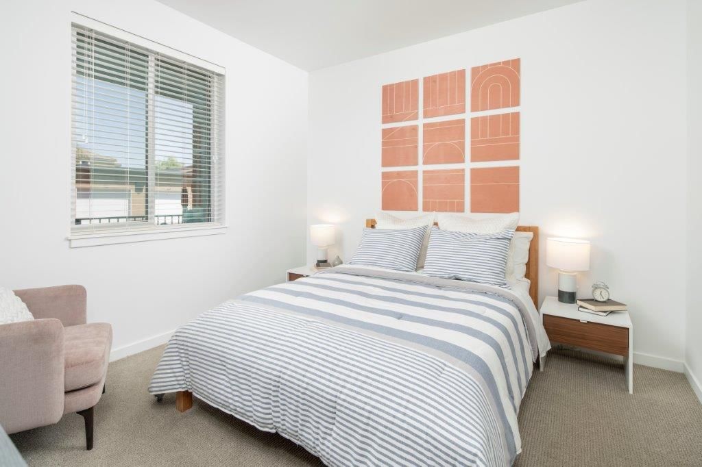 Bedroom in a modern apartment with a striped bedspread, two nightstands, lamps, and wall art.