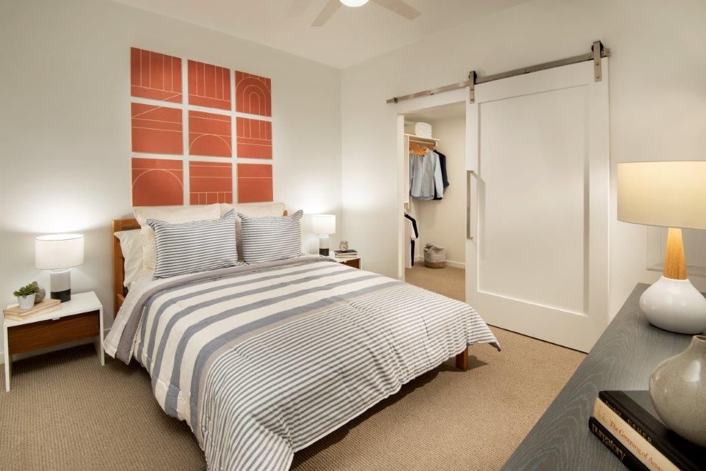 Bedroom in a modern apartment with a bed, two nightstands, dresser, and an open sliding closet.