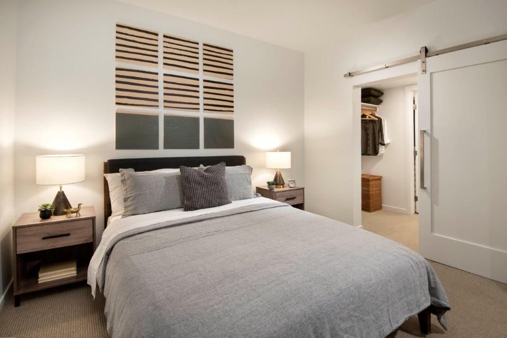 Bedroom in an apartment with a bed, two nightstands, lamps, and an open closet.