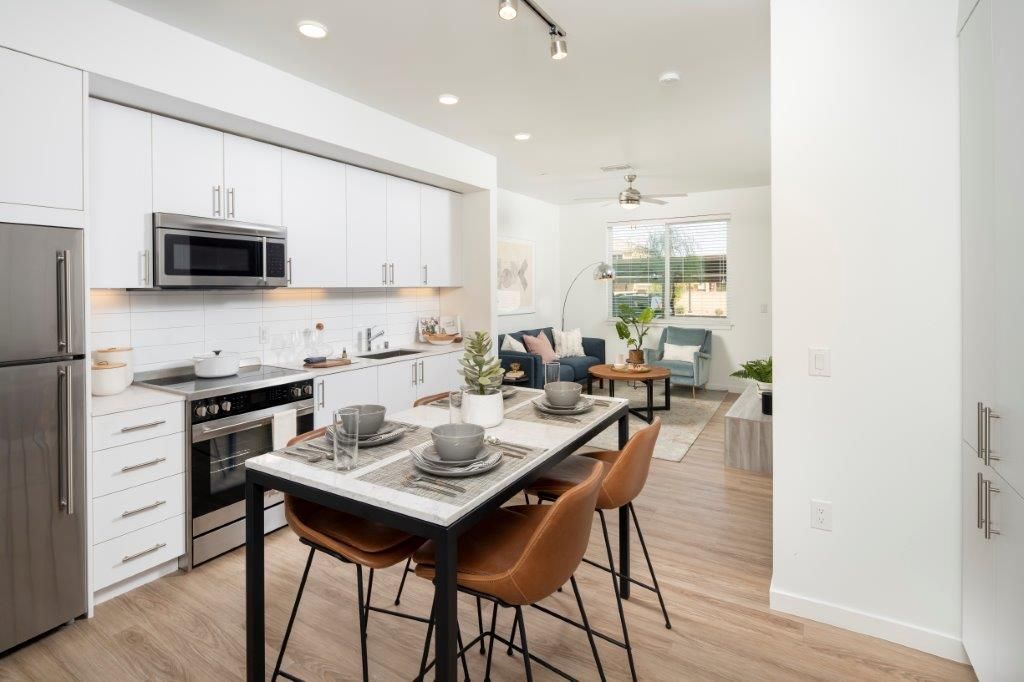 Open-concept kitchen and living area with white cabinets, stainless appliances, and a dining island.