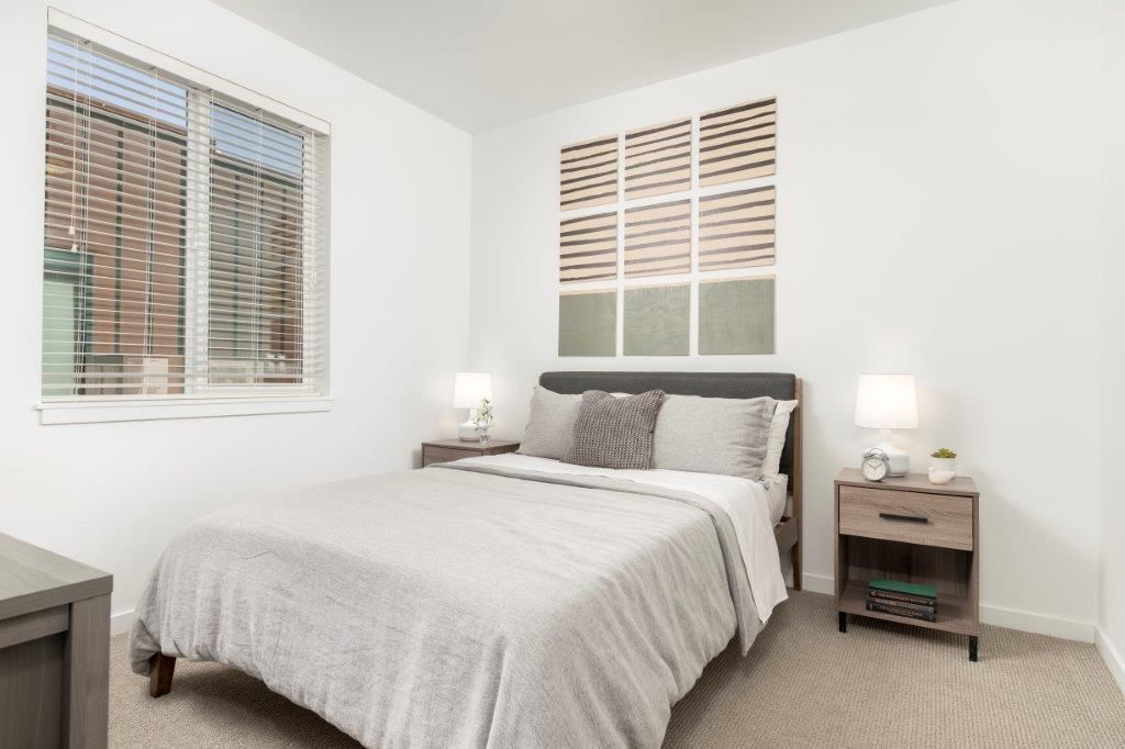 Bedroom interior with a queen bed, two nightstands, lamps, and a window with blinds.