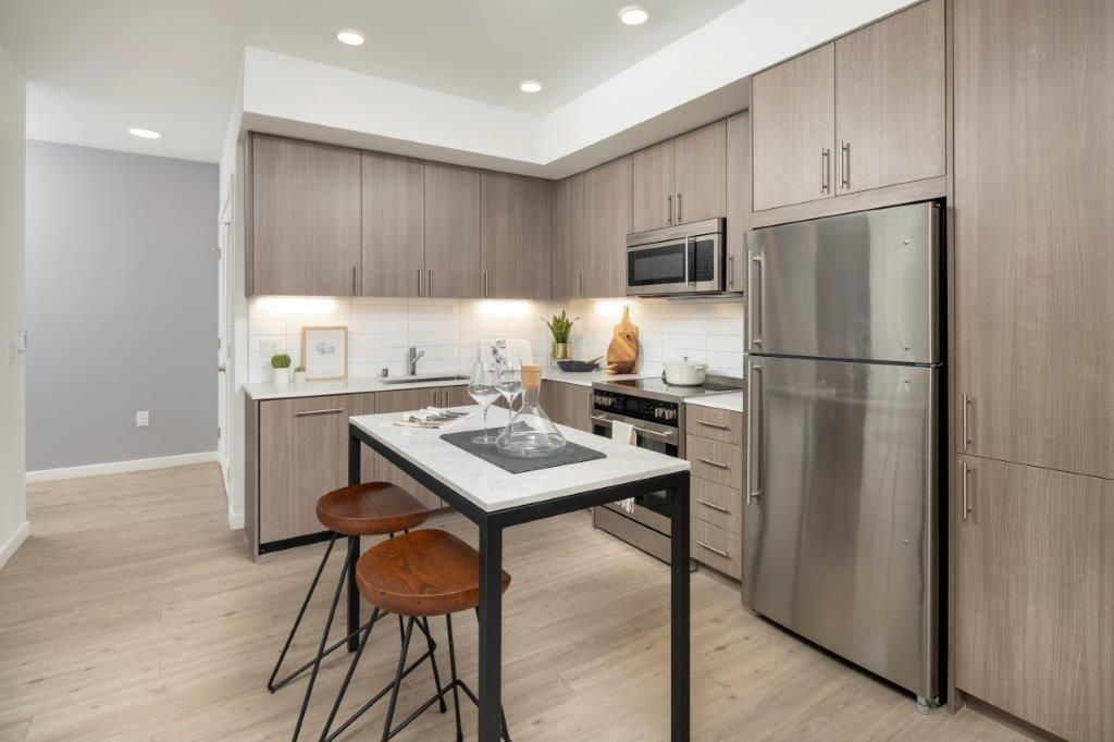 Bright modern apartment kitchen with wood cabinets, stainless steel appliances, and a small island.
