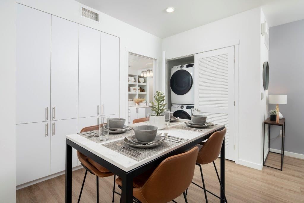 Dining table with place settings in a modern white kitchen; stacked washer and dryer in the laundry alcove.
