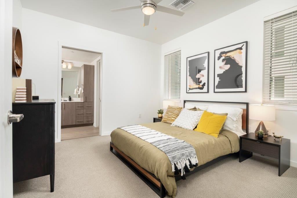 Bedroom in a modern apartment with a bed, two nightstands, and an adjacent bathroom doorway.
