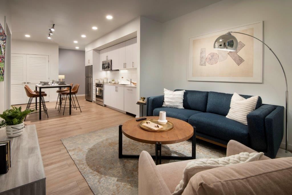 Open-concept living area with a blue sofa, round coffee table, and adjacent kitchen in a modern apartment.