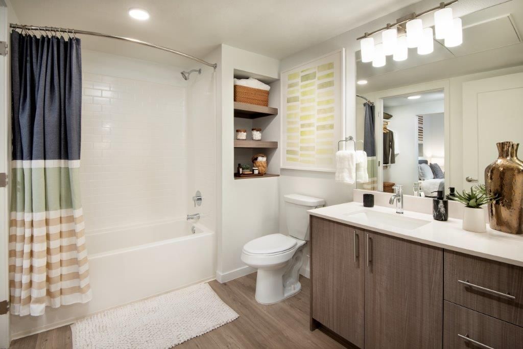 Modern apartment bathroom with tub/shower, toilet, and wood-tone vanity.